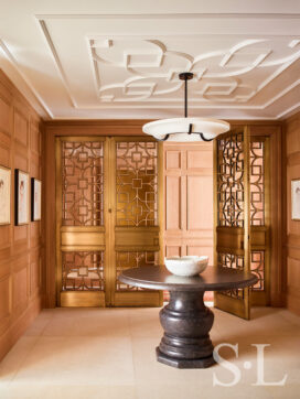 Chicago penthouse entry foyer with cerused oak paneled millwork, a collection of artwork by David Hockney, an iron and plaster pendant light and a Belgian bluestone table