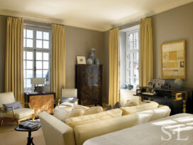 Deco-era duplex apartment primary bedroom view towards seating area with a chinoiserie armoire and Empire writing commode, and view of Lake Michigan out window