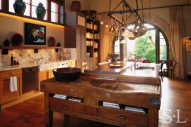 Former artillery shed converted into luxury residence kitchen with large antique Irish butcher-block table and hanging pot rack