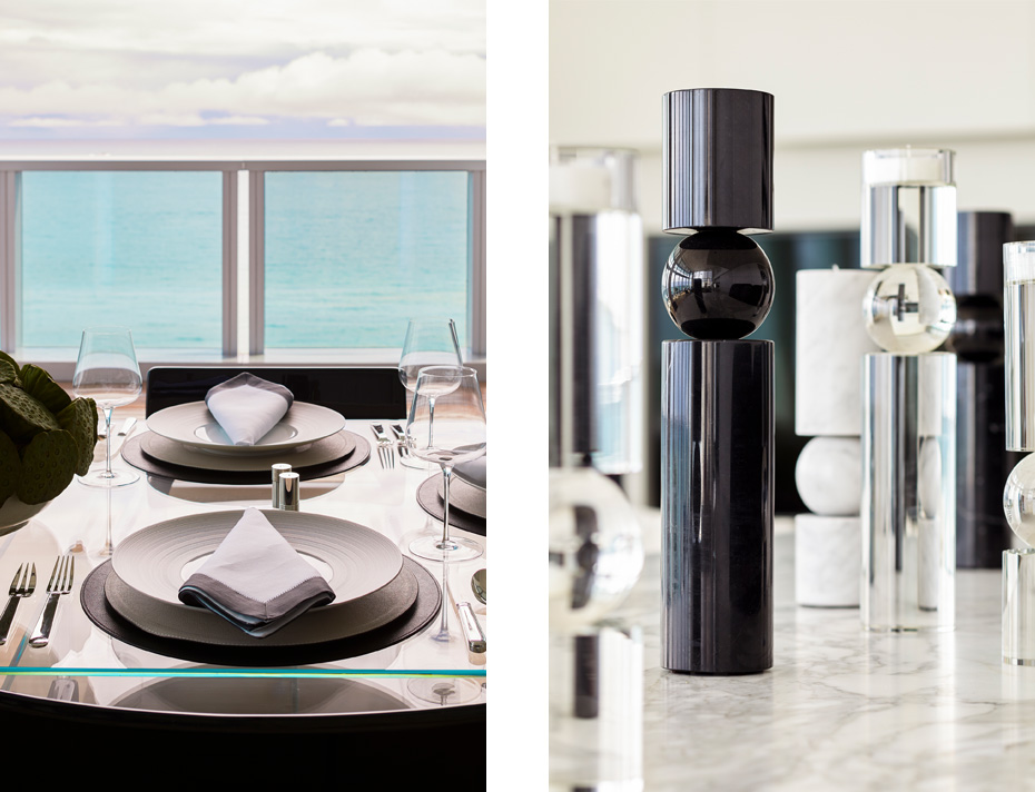 Dining table place setting with ocean and clouds backdrop, next to Fulcrum candlesticks in Nero Marquina Marble, White Carrara marble, and crystal