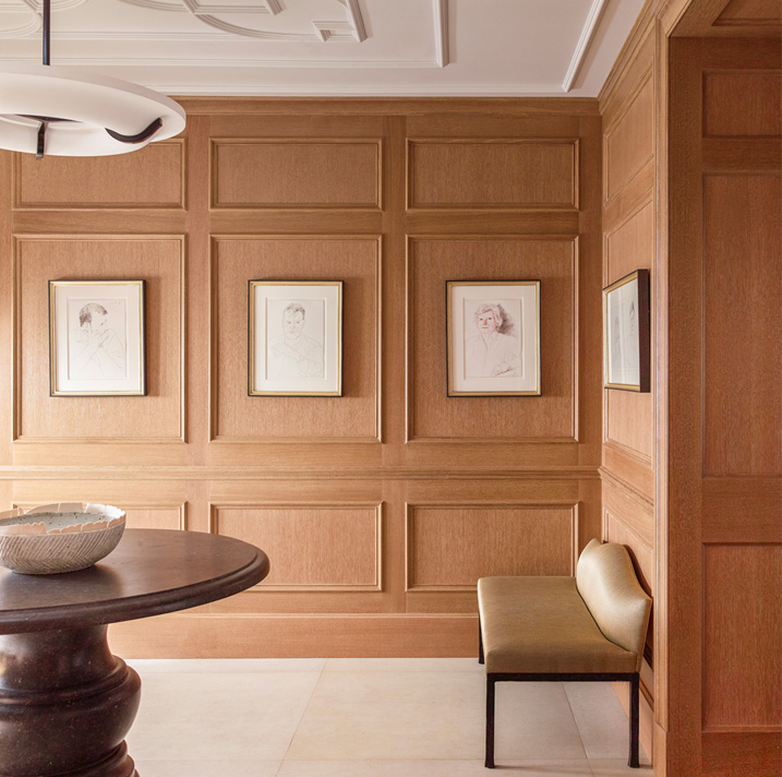Chicago penthouse entry foyer with cerused oak paneled millwork, a collection of artwork by David Hockney, an iron and plaster pendant light and a Belgian bluestone table