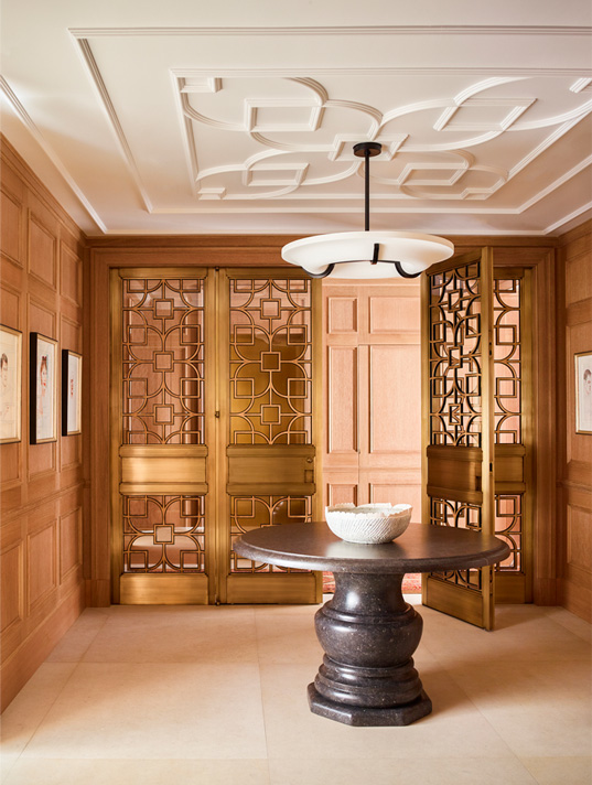 Chicago penthouse entry foyer with cerused oak paneled millwork, a collection of artwork by David Hockney, an iron and plaster pendant light and a Belgian bluestone table