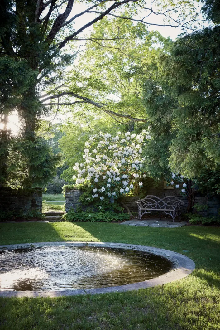 White rhododendron hang over a rustic bench near a reflecting pond on the house's front lawn.